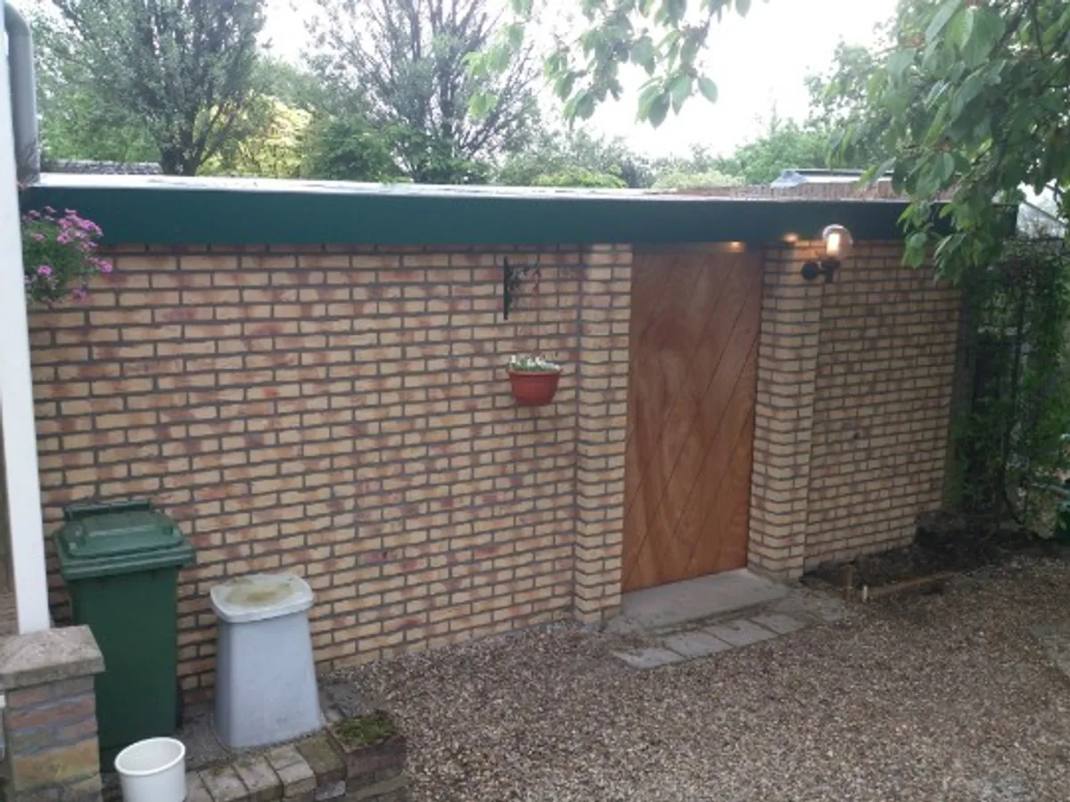 Stenen tuinhuis met houten deur en groen dak